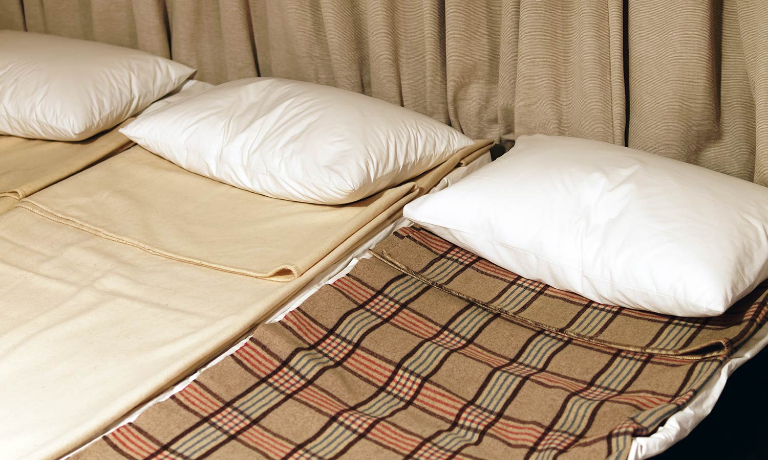 Three small cots next to each other with pillows and thin blankets.