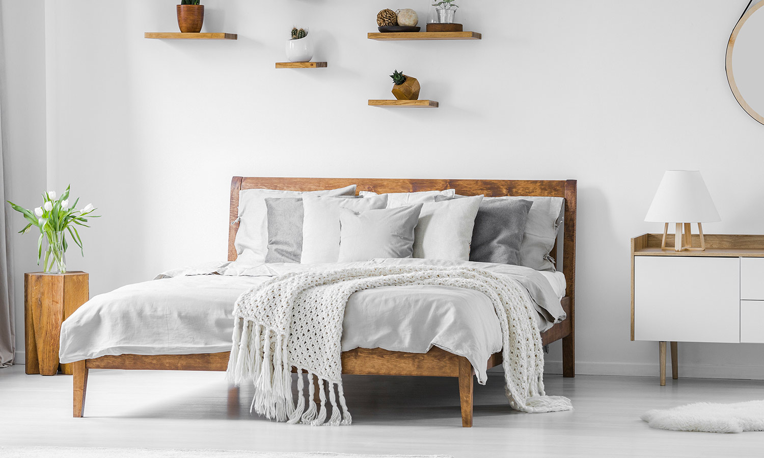 A plain wood-framed bed with modern blankets and pillows on top.