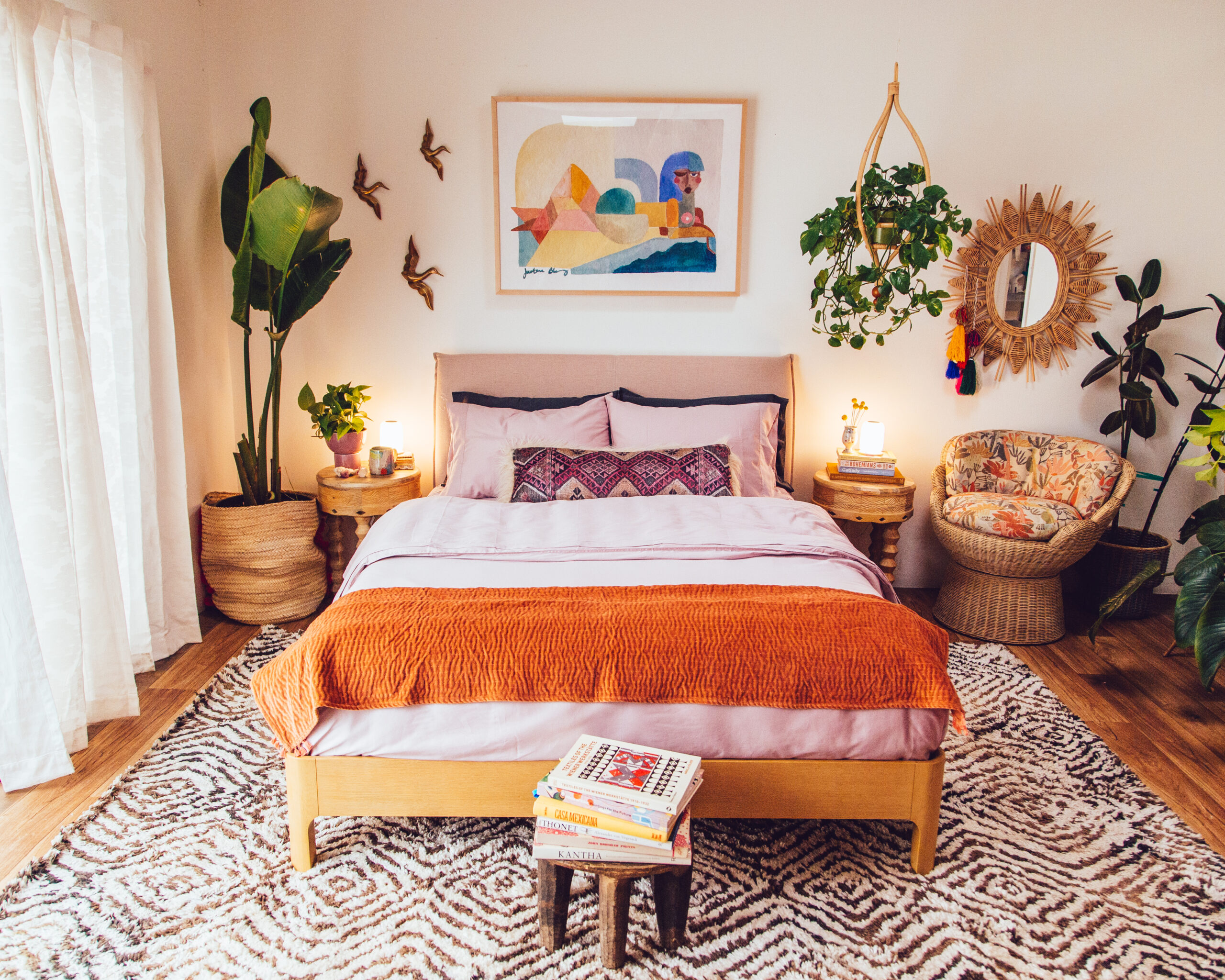 colorful bedroom with plants, pink sheets, and a printed rug